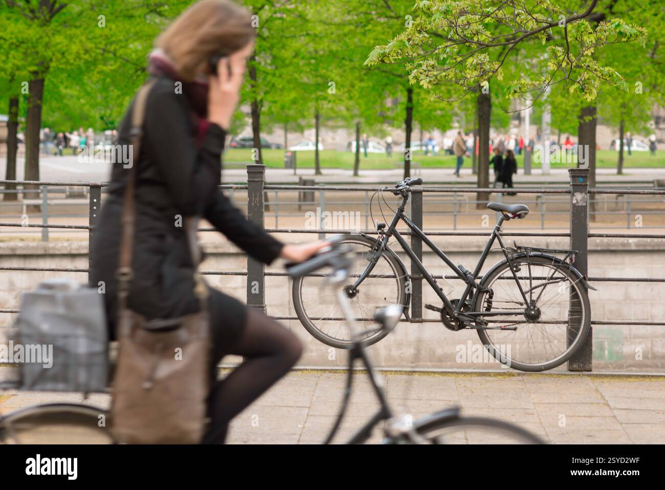 Radfahrerin, Blick auf eine Frau im späten Frühjahr, die mit ihrem Telefon spricht, während sie in der Nähe des Lustgartens im Zentrum Berlins radelt. Stockfoto