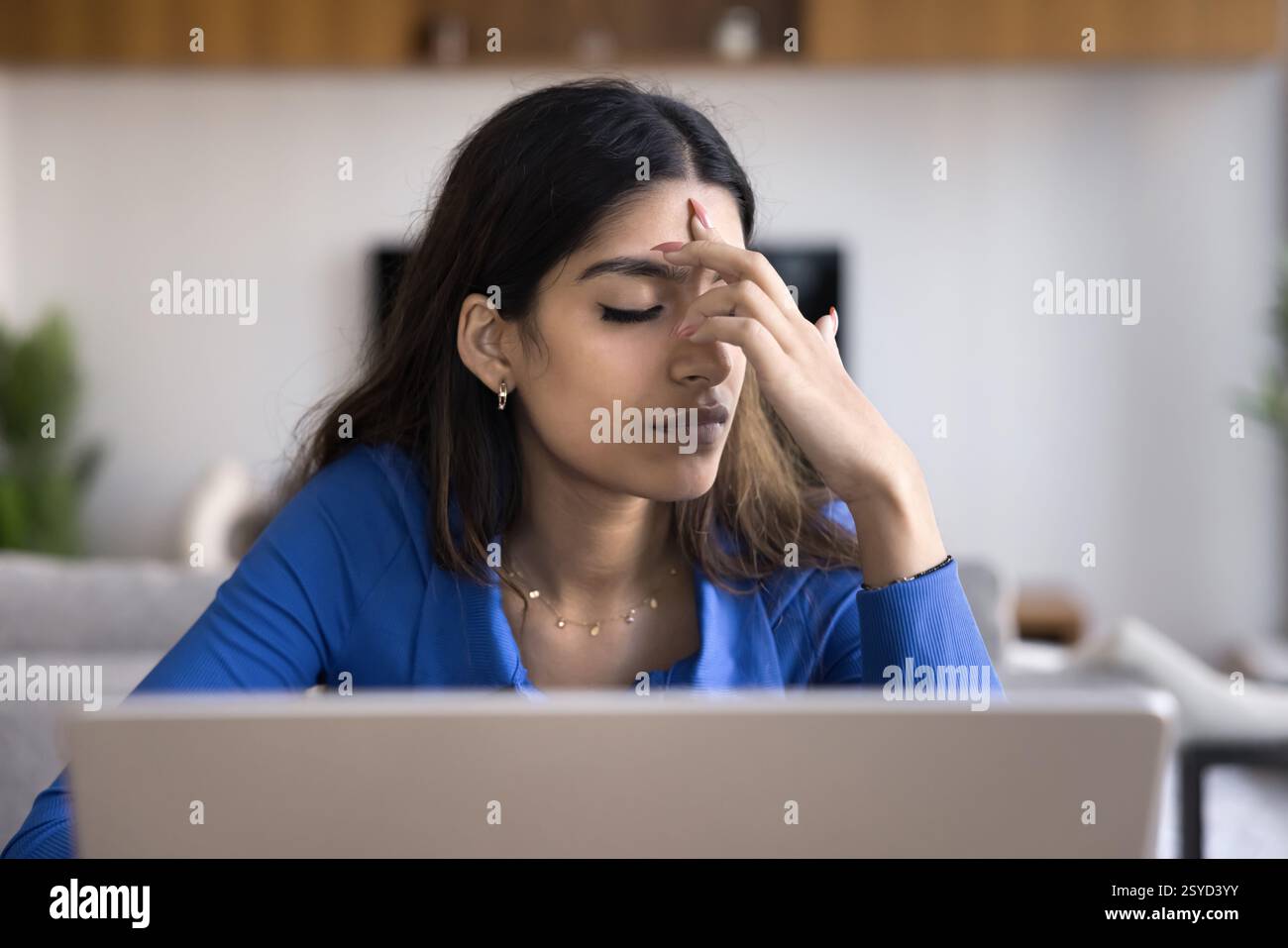 Frau sitzt mit Laptop und Augen geschlossen und merkt sich Informationen Stockfoto