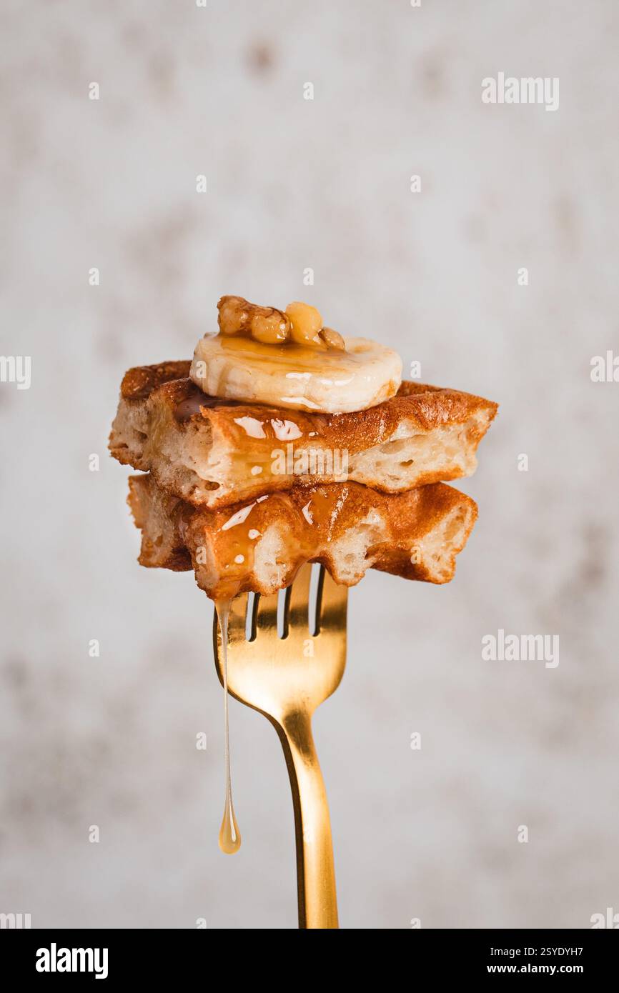 Ein goldener Hauch von Brunch – knusprige Waffeln mit Banane, Walnüssen und einem traumhaften Spritzer Sirup Stockfoto