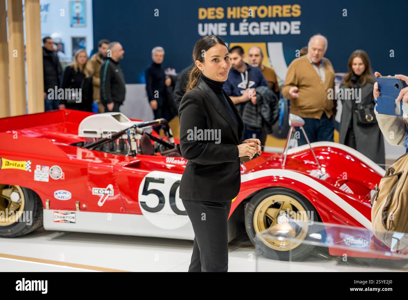 Eine elegante Frau trifft auf eine Automobilausstellung mit einem klassischen Rennwagen im Hintergrund Stockfoto