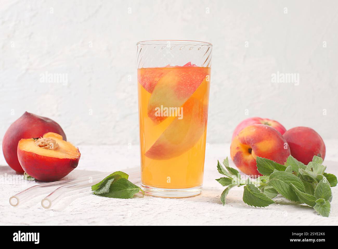 Eistee oder Cocktail mit Pfefferminze und Lobdom, Rezept für erfrischendes Sommergetränk. Glas mit Pfirsichfrucht-Limonade auf leichtem Betontisch, Entgiftungsdiät Stockfoto