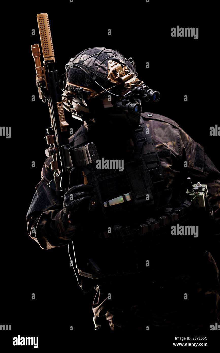 Bewaffneter Soldat mit umfassender taktischer Ausrüstung, Gewehr und Nachtsichtbrille, vorbereitet für eine verdeckte Militäroperation bei schlechten Lichtverhältnissen Stockfoto