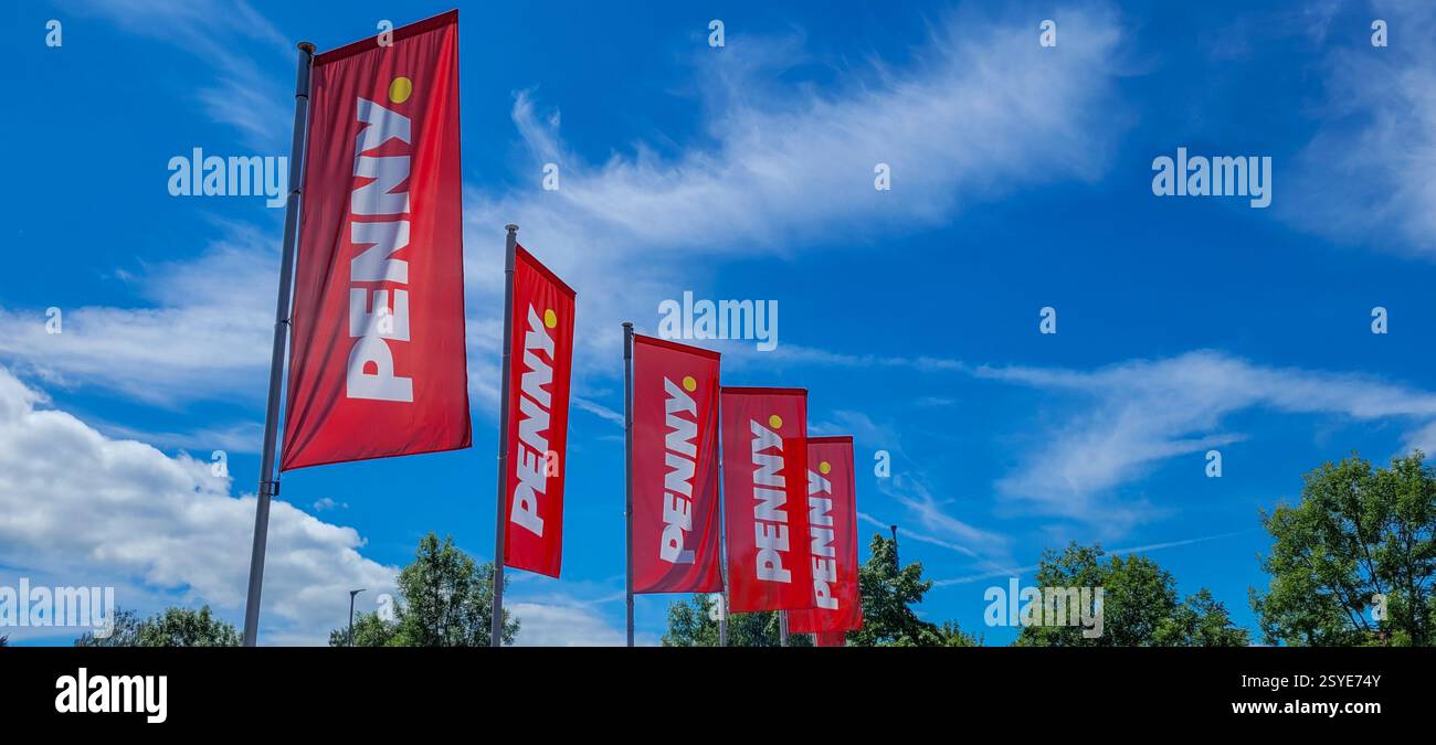 Penny Market Logo zwischen dem hellblauen Himmel, weißen Wolken und grünen Dreien an sonnigem Tag. Mai 2024. Markdorf, Deutschland. Stockfoto