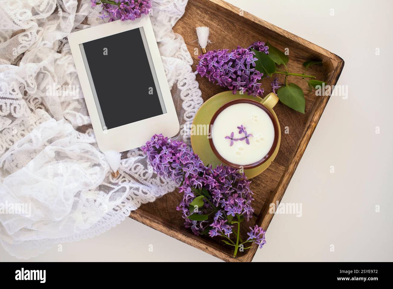 Sommer- oder Frühjahrsheim gemütliche Komposition mit Spitze, blühenden lilafarbenen Zweigen, E-Book mit Kopierraum und einer Tasse Milch. Vorlage für feminine Blogs. Stockfoto