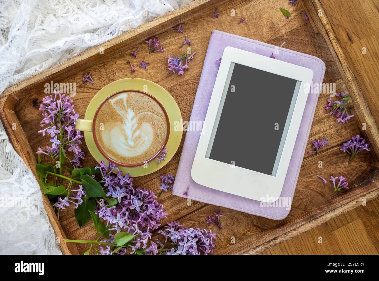 Sommer- oder Frühjahrsheim gemütliche Komposition mit Spitze, blühenden lilafarbenen Zweigen, E-Book mit Kopierraum und einer Tasse Kaffee. Vorlage für feminine Blogs. Stockfoto