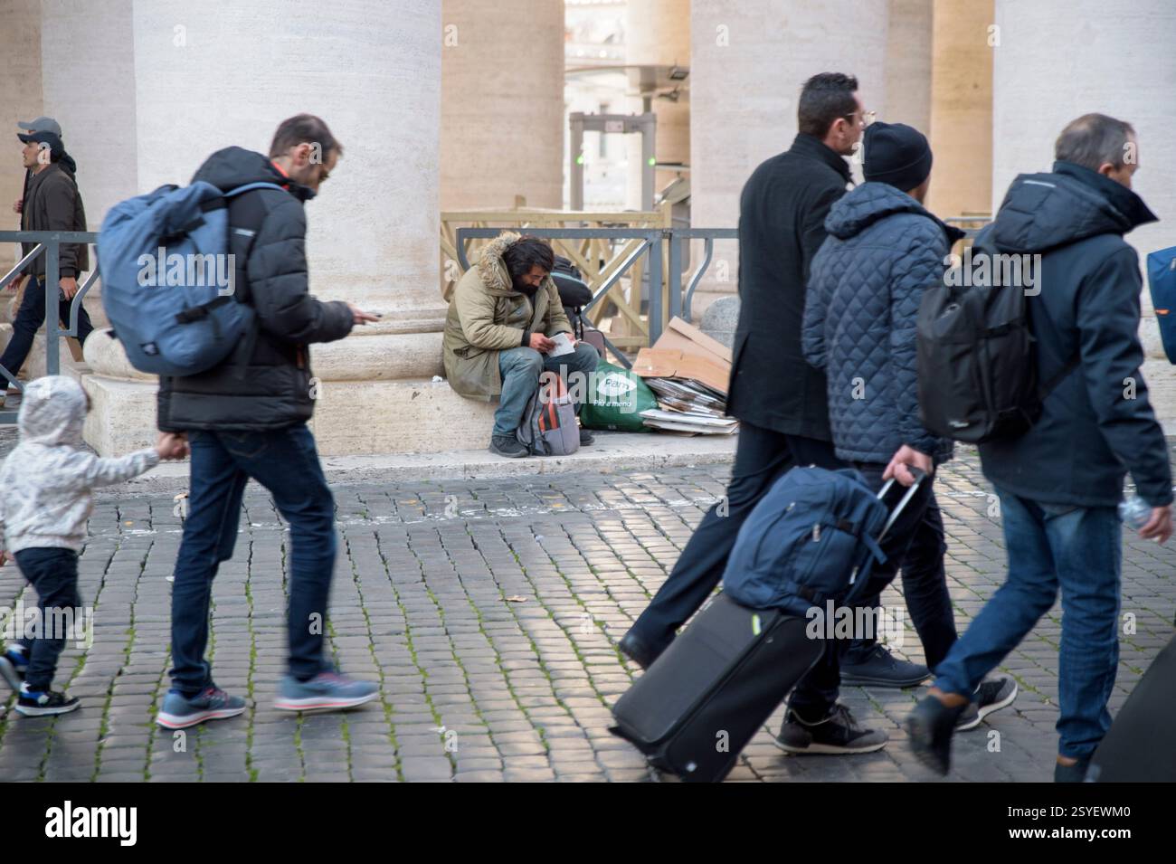 Vatikanstadt, Vatikanstaat. Februar 2025. Touristen kommen und gehen, während ein Obdachloser ein Buch liest, das unter Berninis Kolonnade auf den Abend wartet, wo er die Nacht im Vatikan in Rom verbringen wird. Jeden Abend empfängt die Bernini-Kolonnade über 70 Obdachlose, die dann früh am Morgen verlegt werden. Viele haben psychiatrische Probleme und verweigern die Aufnahme in angemessenere Einrichtungen. Einige Betreiber, die sich mit der Sicherheit des Platzes befassen, melden auch Vorfälle mit Touristen. (Kreditbild: © Marcello Valeri/ZUMA Press Wire) NUR REDAKTIONELLE VERWENDUNG! Nicht für kommerzielle ZWECKE! Stockfoto