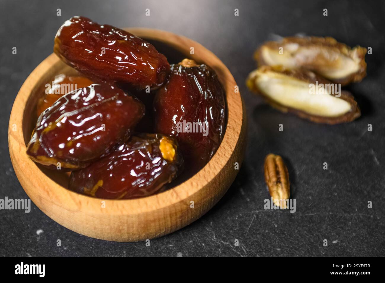 Traditionelle Ramadan-Datteln in Holzschale auf schwarzem Hintergrund Stockfoto