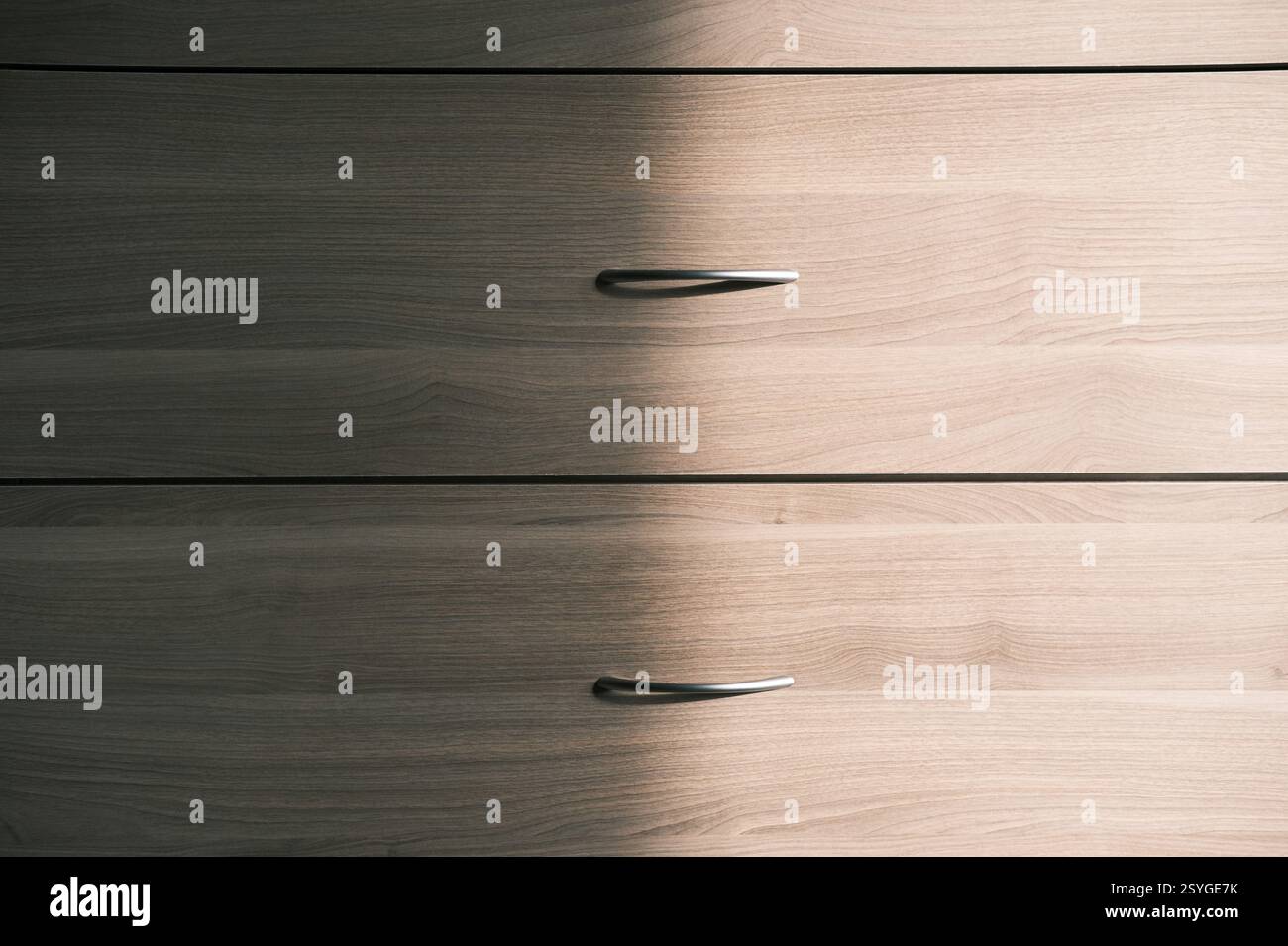 Vorderansicht der Holzkommode, halb sonnenbeleuchtet, Schubladen mit Griffen. Beige, gräuliche, silberfarbene Eschenfarbe. Organisation und Ordnung zu Hause, Entwirren. Sta Stockfoto