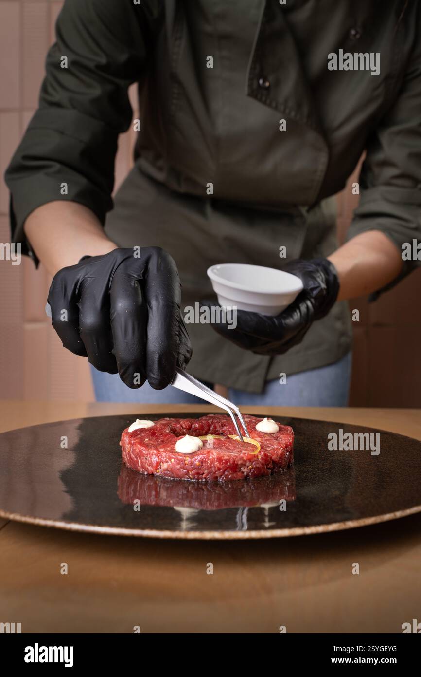 Ein professioneller Küchenchef bereitet in einer gehobenen Restaurantküche ein Gourmet-Rindfleisch-Tartar zu, das sich auf Präzision und Präsentation der Speisen konzentriert. Stockfoto