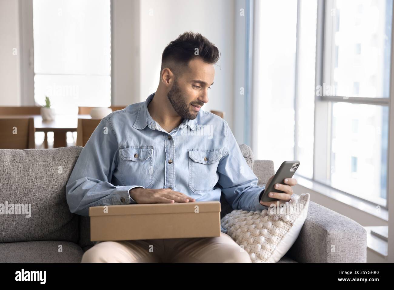 Mann, der die Box hält, mit dem Smartphone, überprüfen Sie die Lieferdetails Stockfoto