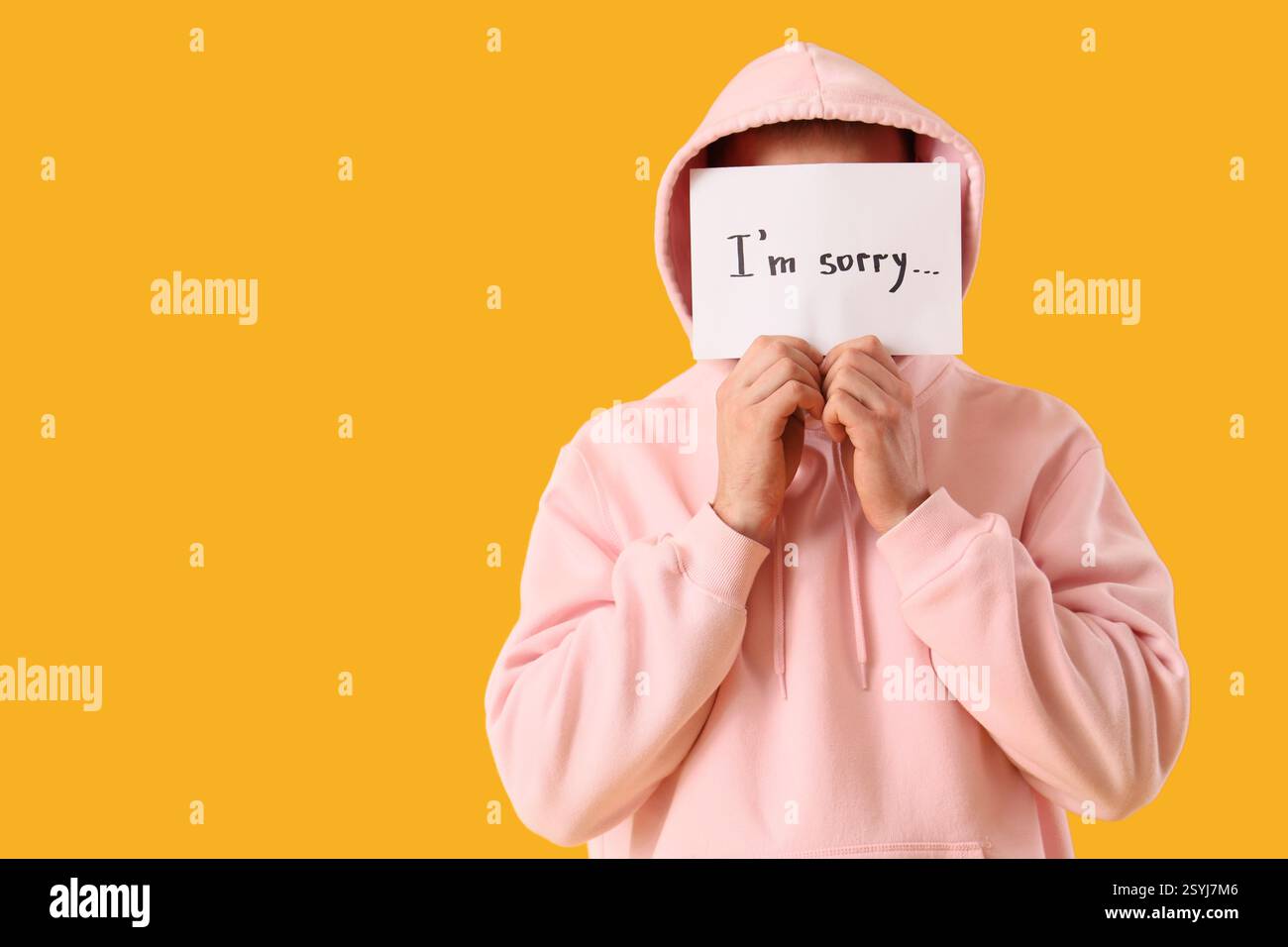 Junger Mann, der Papier hält, mit Text "TUT MIR LEID" auf orangem Hintergrund Stockfoto