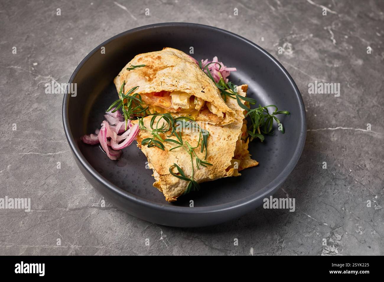Eine Nahaufnahme einer leckeren Quesadilla mit Käse, Kräutern und Zwiebeln, präsentiert auf einem dunklen Teller mit Steinhintergrund, mexikanisches Lebensmittelkonzept Stockfoto