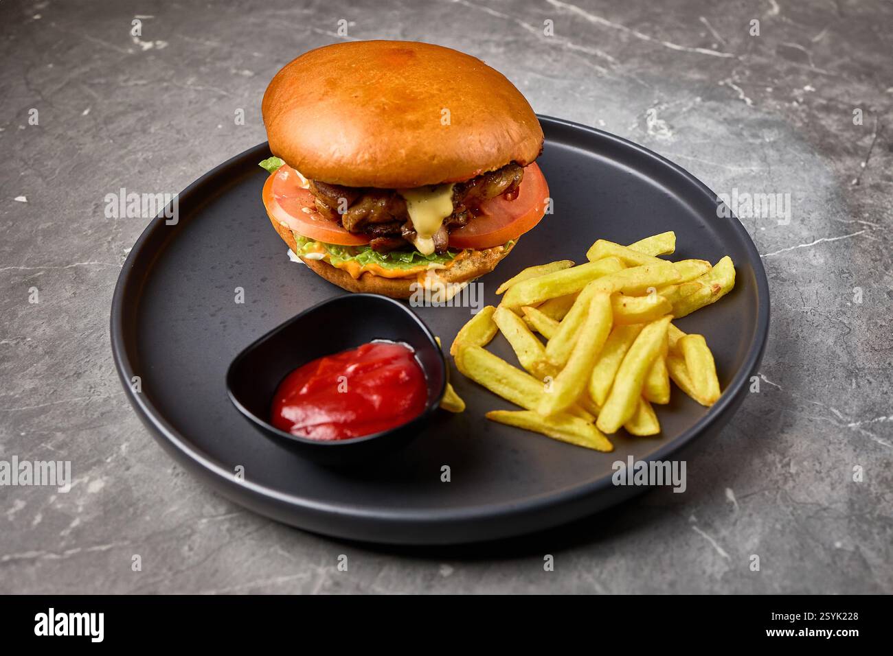 Leckerer Burger mit Salat, Tomate, serviert mit Pommes und roter Sauce auf einem schwarzen Teller, Fast Food Konzept Stockfoto