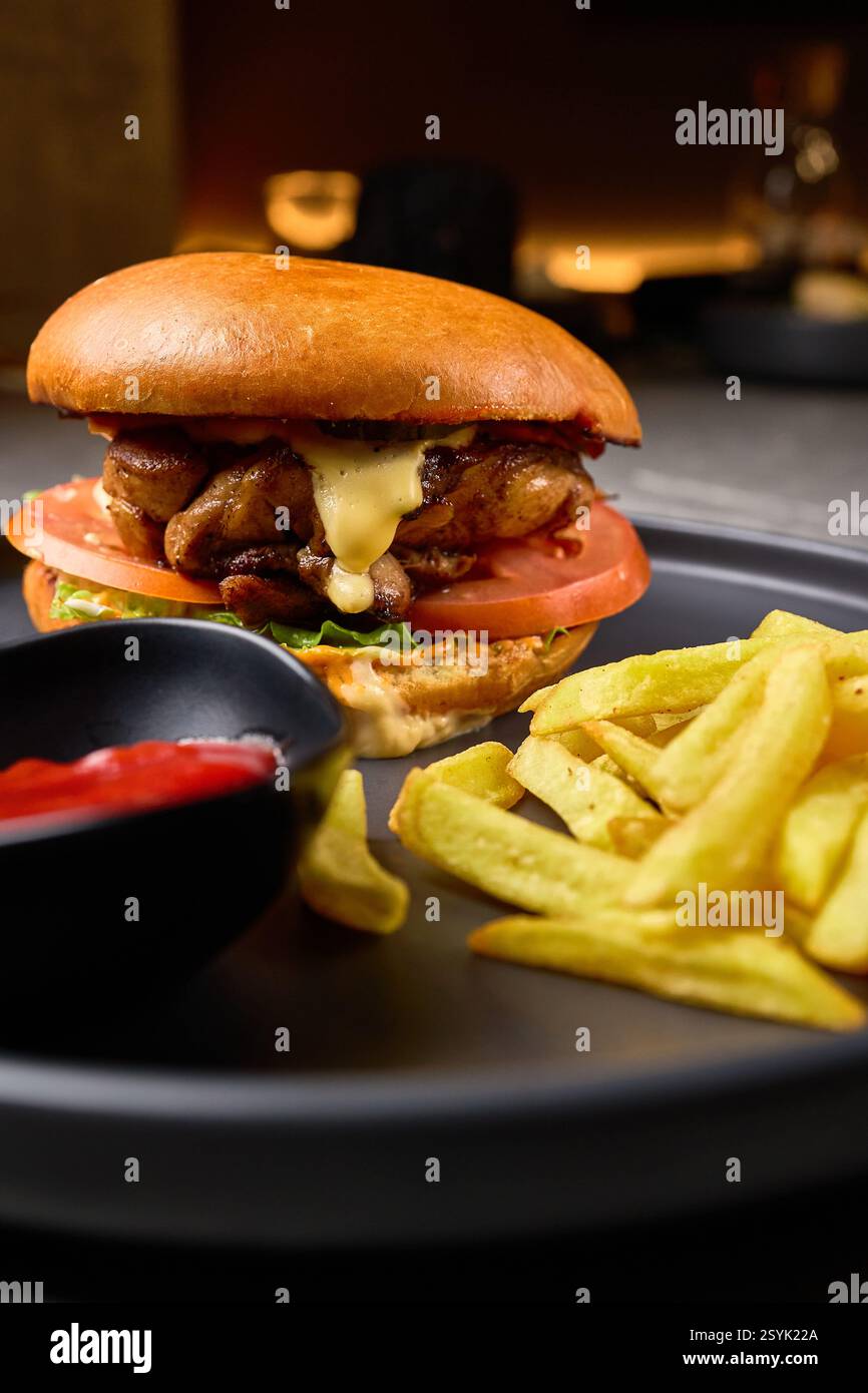 Saftiger Chicken Cheeseburger mit frischem Gemüse, knusprigen Pommes und Ketchup auf Black Plate, eine Idee für Gourmet-Fast-Food-Mahlzeiten, köstliches Konzept Stockfoto