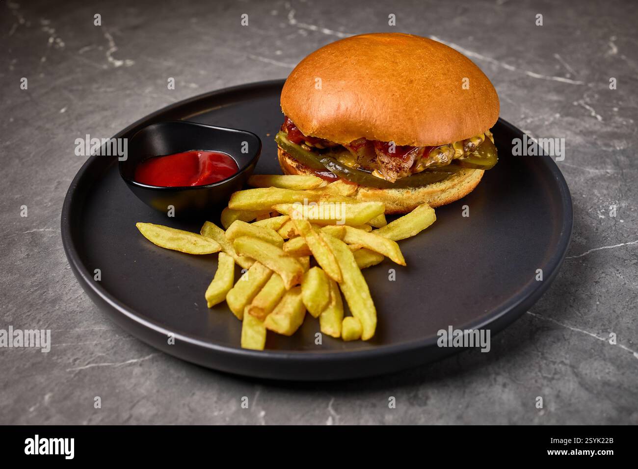 Appetitliche Essenspräsentation mit Pommes, Gourmet-Burger, Ketchup, serviert auf schwarzem Teller, köstlichem Mahlzeitkonzept Stockfoto