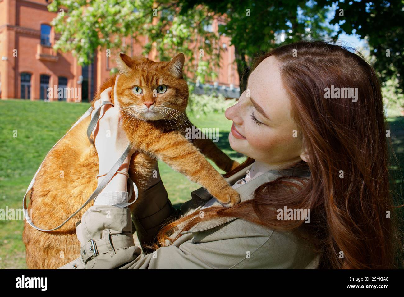 Ingwermädchen mit Ingwerkatze an der Leine im Park Stockfoto