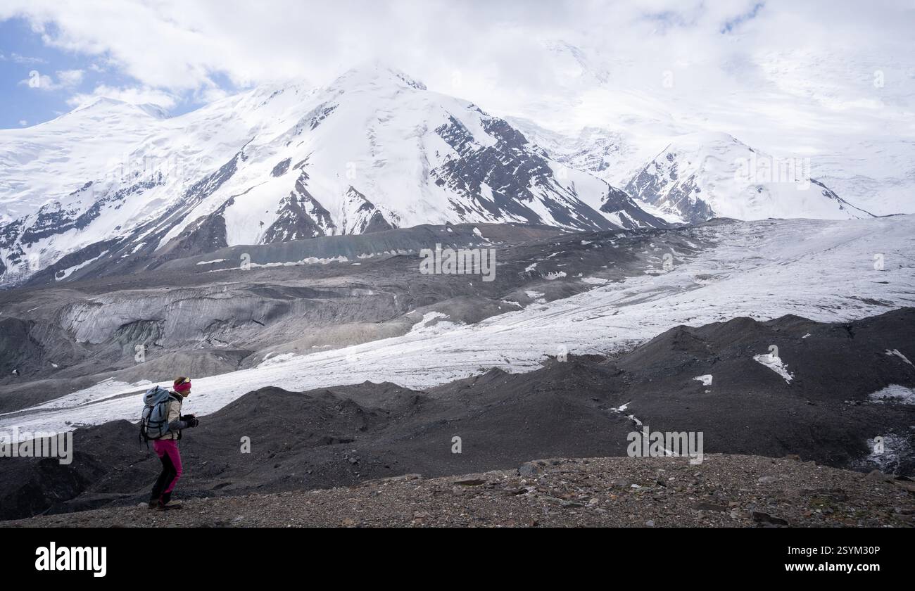 Weibliche Wanderer, die bergauf mit riesigen schneebedeckten Bergen und Gletschern im Hintergrund laufen, Pamir, Kirgisistan Stockfoto