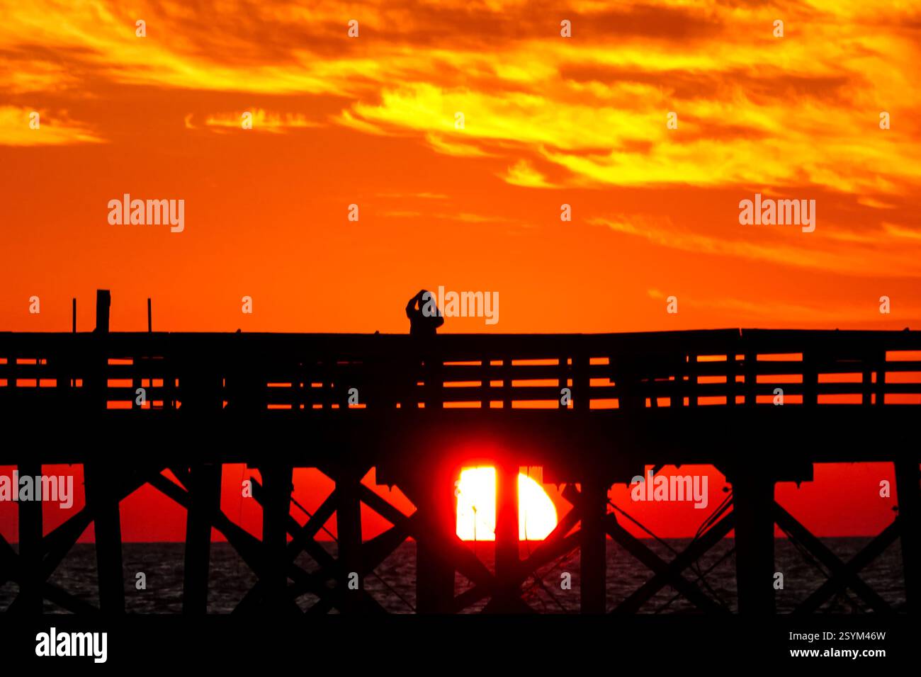 Isle Of Palms, Usa. März 2025. Eine Person, die vom Sonnenaufgang über dem Atlantischen Ozean geschildert wird, beobachtet vom Isle of Palms Pier am Front Beach, 1. März 2025 in Isle of Palms, South Carolina. Eine allmähliche Erwärmung bis in die 70er Jahre wird sich nach einem harten Winter im Tiefland fortsetzen. Quelle: Richard Ellis/Richard Ellis/Alamy Live News Stockfoto