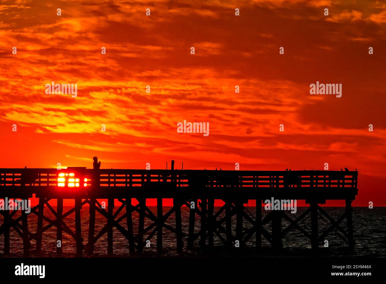 Isle Of Palms, Usa. März 2025. Eine Person, die vom Sonnenaufgang über dem Atlantischen Ozean geschildert wird, beobachtet vom Isle of Palms Pier am Front Beach, 1. März 2025 in Isle of Palms, South Carolina. Eine allmähliche Erwärmung bis in die 70er Jahre wird sich nach einem harten Winter im Tiefland fortsetzen. Quelle: Richard Ellis/Richard Ellis/Alamy Live News Stockfoto