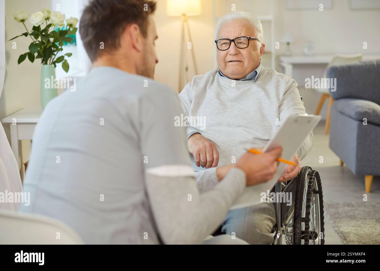 Krankenschwester oder Pflegekraft zeigt Testergebnisse für älteren behinderten Mann im Rollstuhl im Pflegeheim Stockfoto
