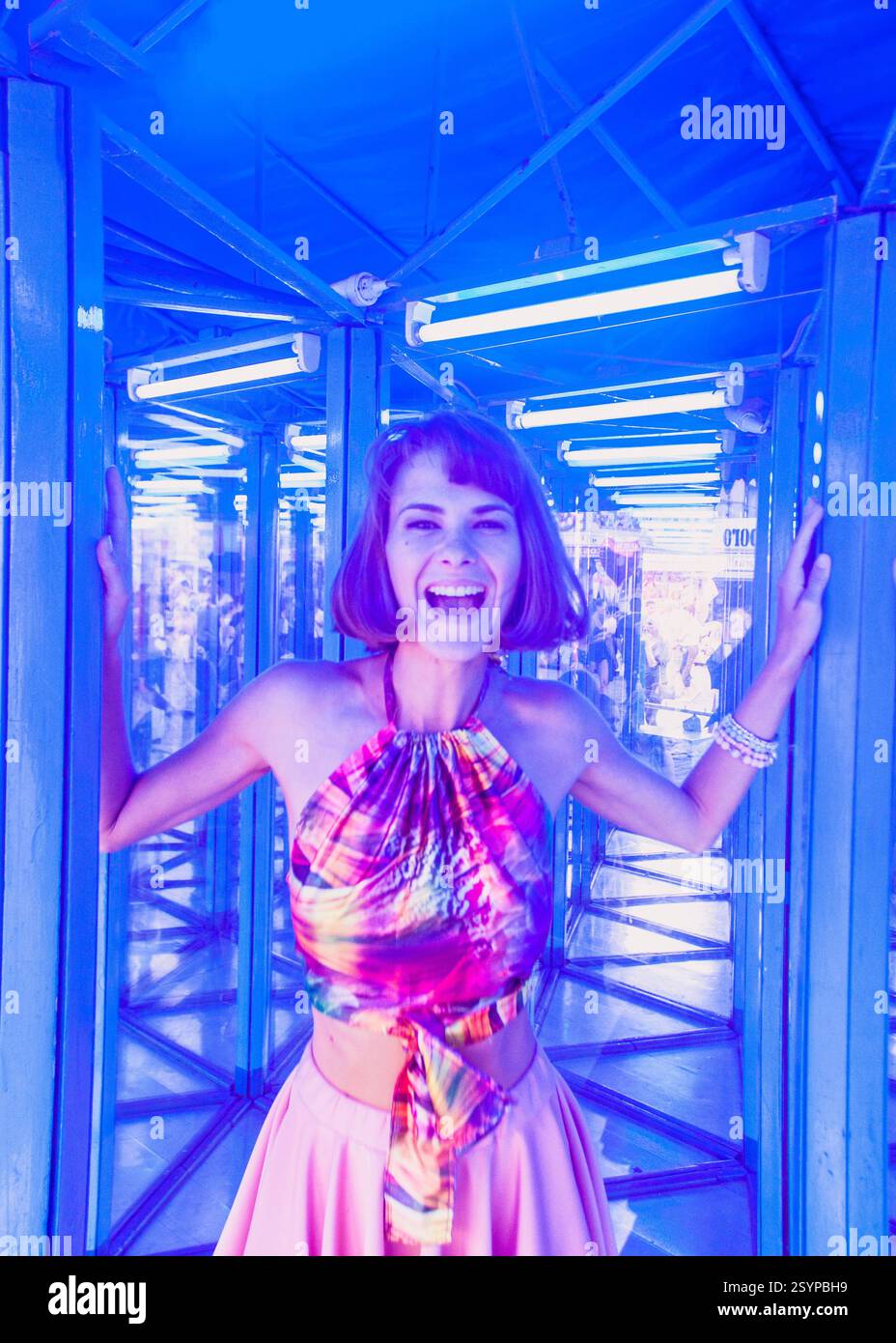 Schöne junge Frau flirtet und interagiert mit einer Lanze der Kamera in einem Spiegellabyrinth oder Glashaus im Vergnügungspark. Sie hat Spaß und ist glücklich Stockfoto