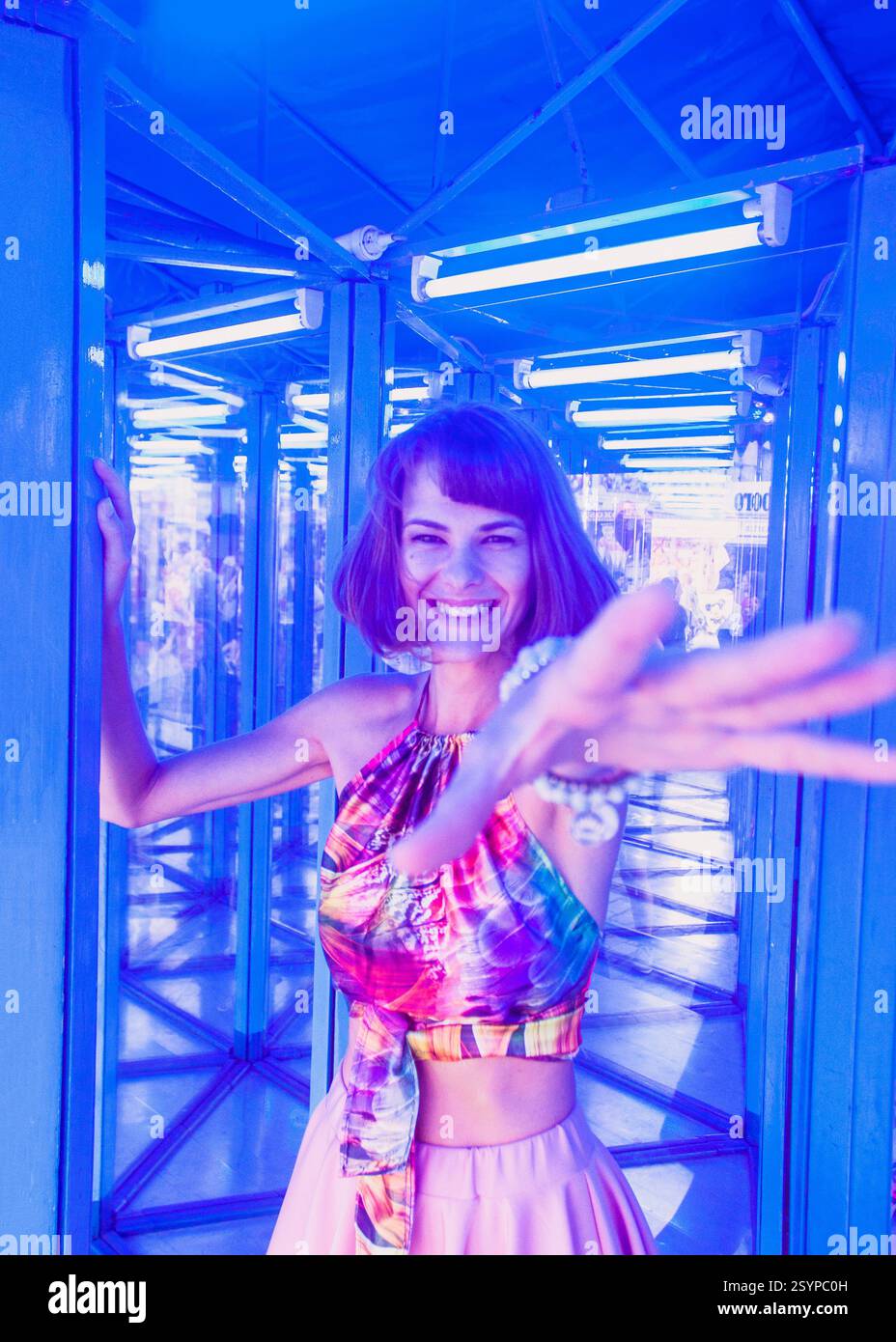 Schöne junge Frau posiert mit der Hand und versucht, die Kamera in einem Spiegellabyrinth oder einem Glashaus im Vergnügungspark zu erreichen. Sie hat lustige, glückliche Gefühle. Stockfoto