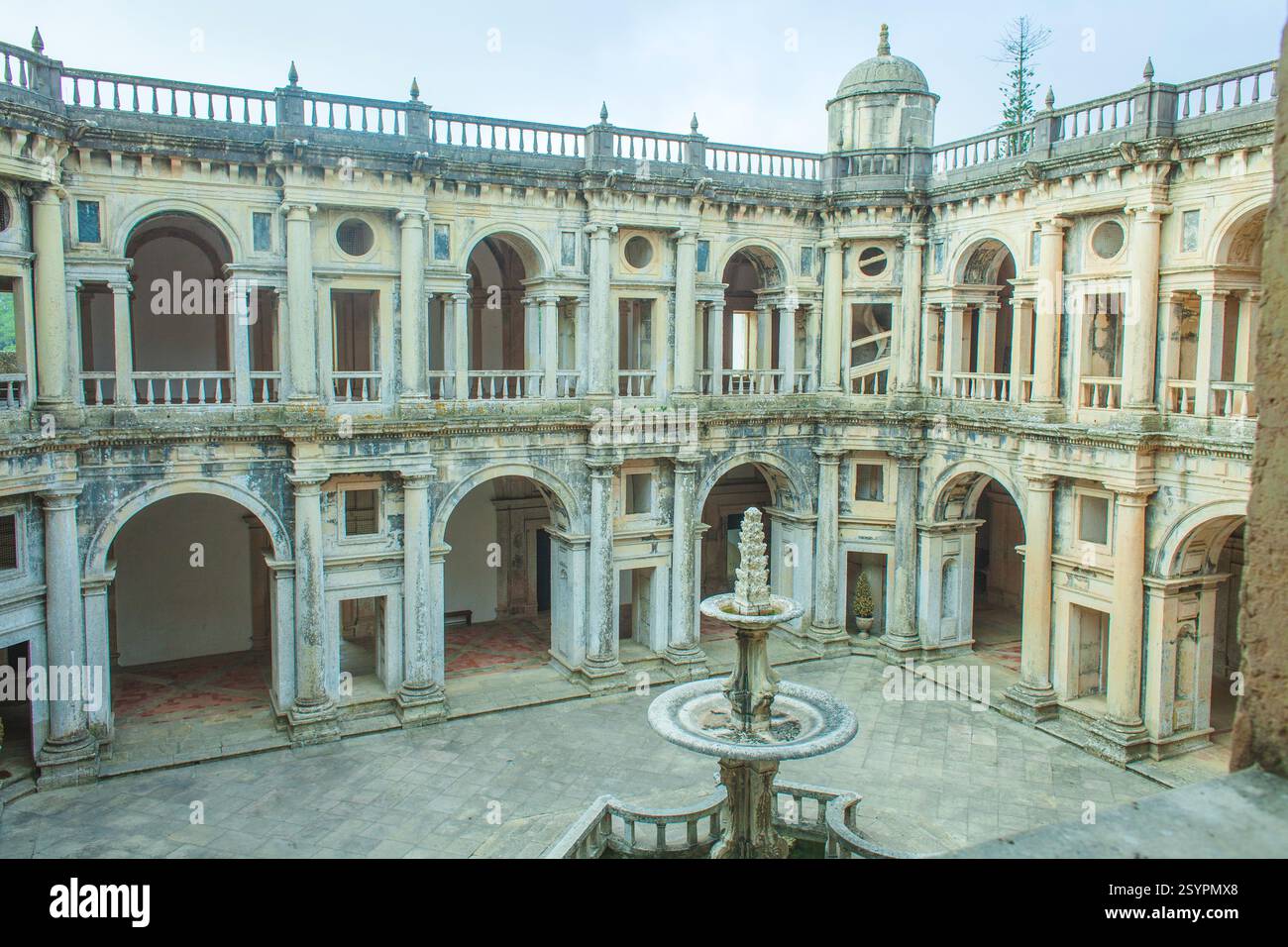 Fesselnder Blick aus der Vogelperspektive auf einen historischen Klosterhof mit symmetrischem Layout mit bogenförmigen Kreuzgängen, einem zentralen Brunnen und üppigem Grün Stockfoto