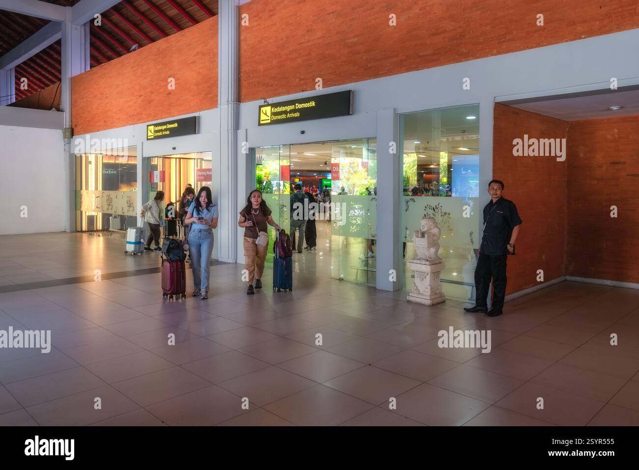 Bali, Indonesien, 9. Oktober 2024 Reisende am geschäftigen Flughafen I Gusti Ngurah Rai werden von freundlichen Mitarbeitern begrüßt, wenn sie mit Gepäck im geldautomaten laufen Stockfoto