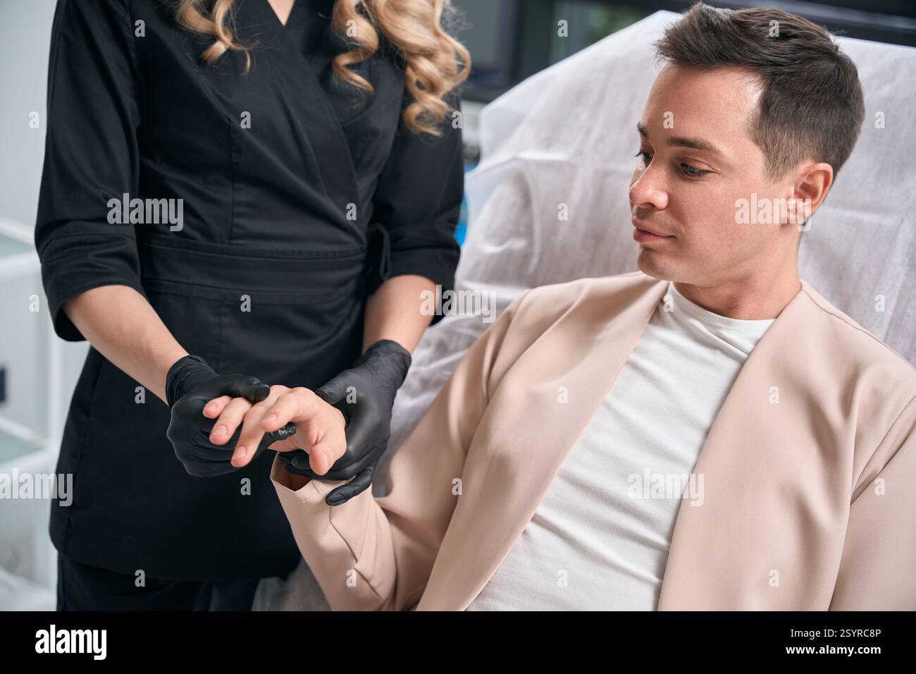 Kosmetikerin in Gummihandschuhen, die männliche Kundenhände überprüft Stockfoto