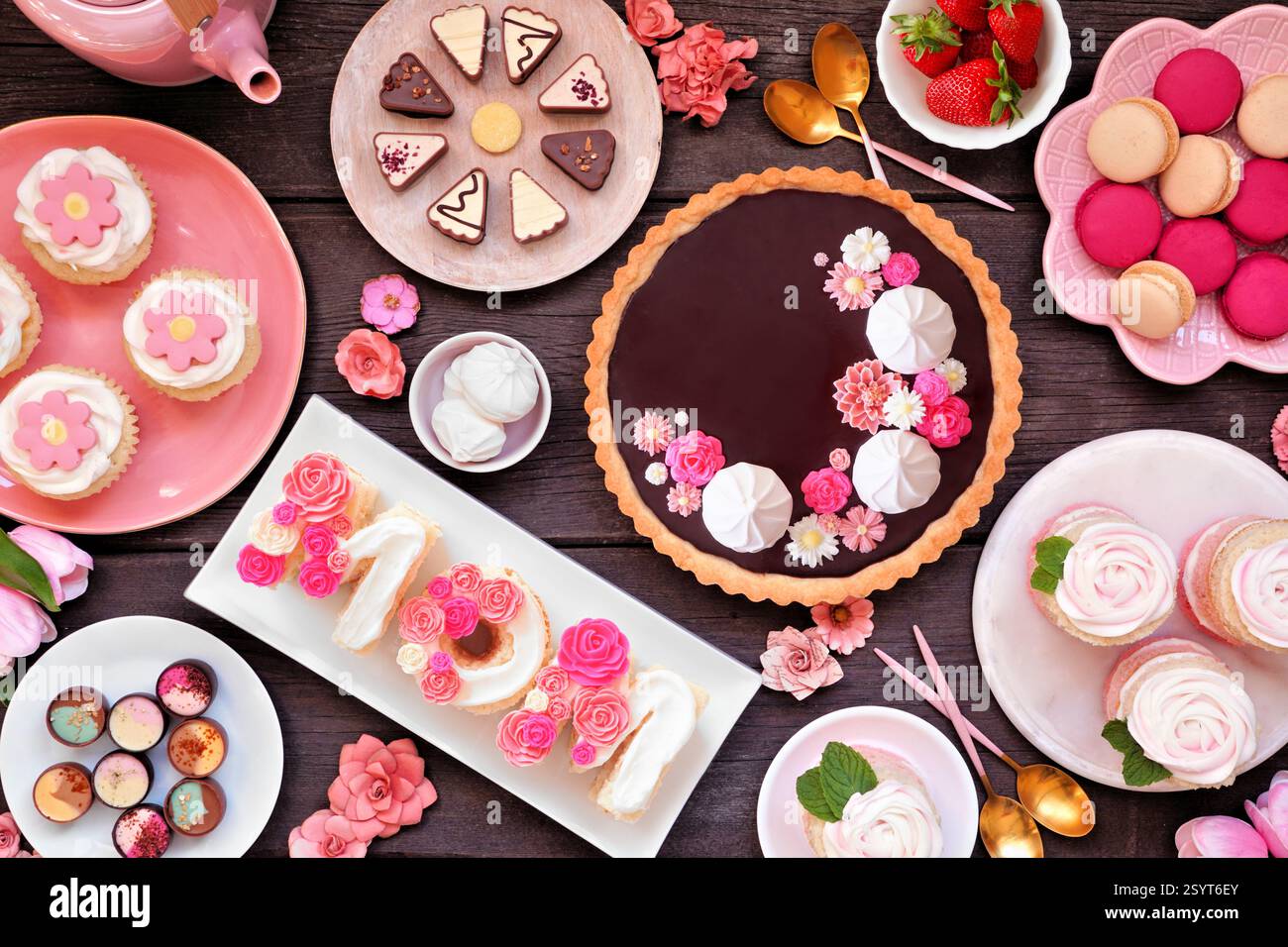 Mothers Day Tischszene mit einer Auswahl an Desserts und Süßigkeiten. Draufsicht auf dunklem Holzhintergrund. Rosafarbenes Blumenmotiv. Stockfoto