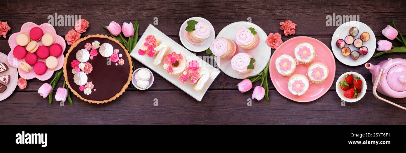 Mothers Day Tischszene mit einer Auswahl an Desserts und Süßigkeiten. Oben auf einem dunklen Holzbanner Hintergrund. Rosafarbenes Blumenmotiv. Stockfoto