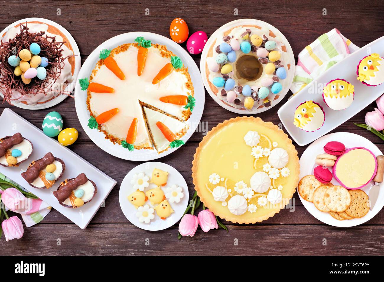 Ostern oder Frühling Dessert Esstisch Tisch Szene. Blick von oben über dunklem Holzhintergrund. Zitronentorte, Cupcakes, Osterei und Karottenkuchen und eine Auswahl Stockfoto