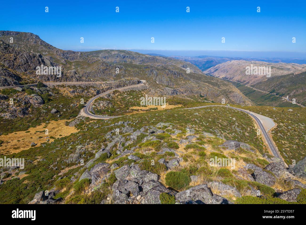 Eine gewundene Straße schlängelt sich durch eine bergige Landschaft mit karger Vegetation unter einem klaren blauen Himmel und zeigt einen malerischen Bergpass Stockfoto