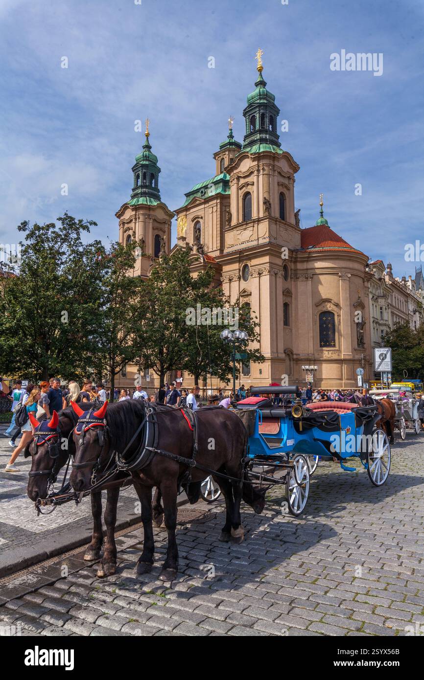 Ein breiter Kopfsteinpflasterplatz in einer europäischen Stadt mit einer historischen Kirche mit Doppeltürmen, kunstvollen Statuen und einem Kuppelgebäude unter bewölktem Himmel. Stockfoto