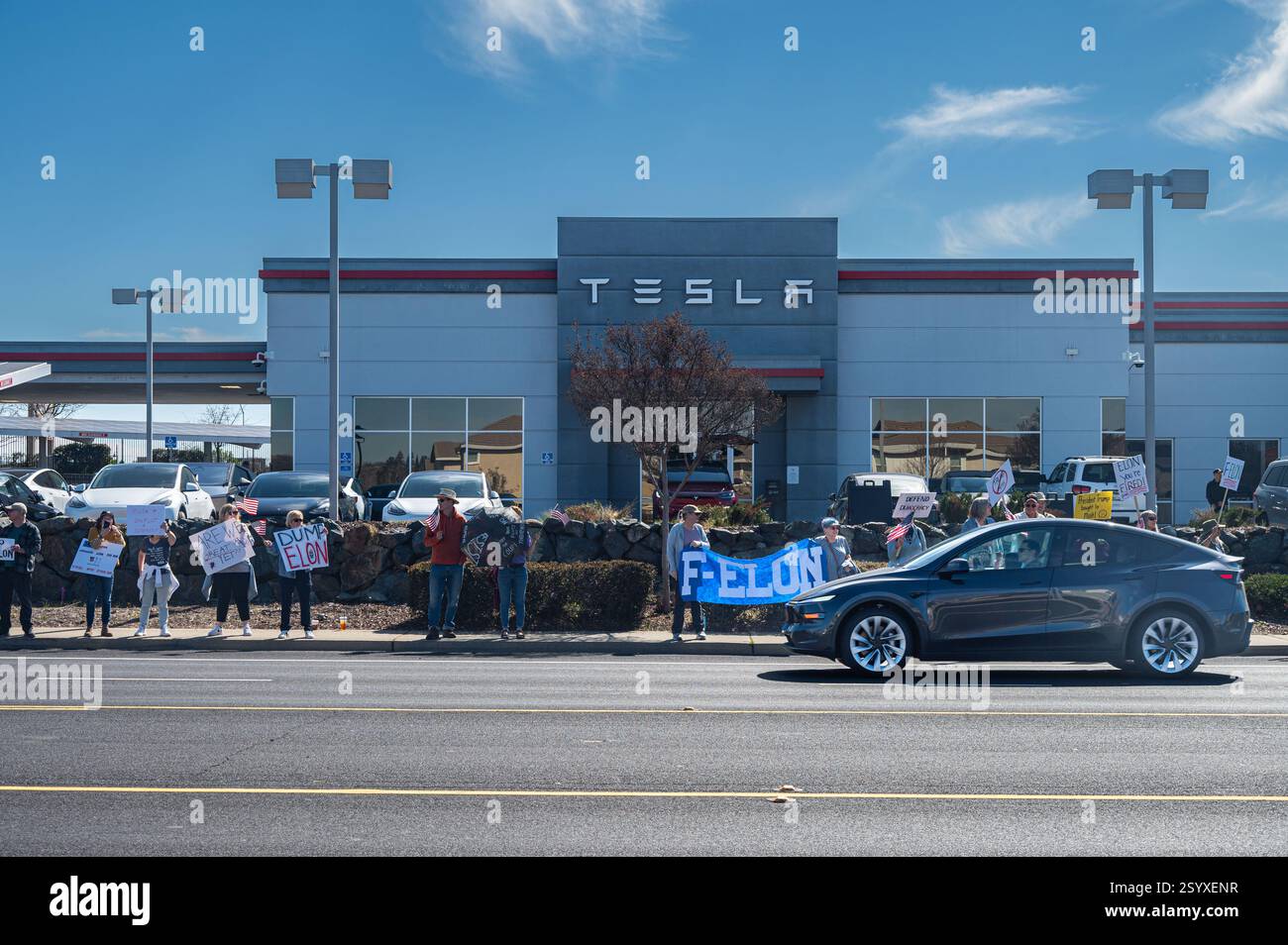 Ein Tesla Auto fährt an einem Tesla-Protest in einem Tesla-Händlerbetrieb vorbei, in dem Demonstranten Schilder wie F-Elon halten, die sich auf den Leiter des Unternehmens beziehen. Stockfoto