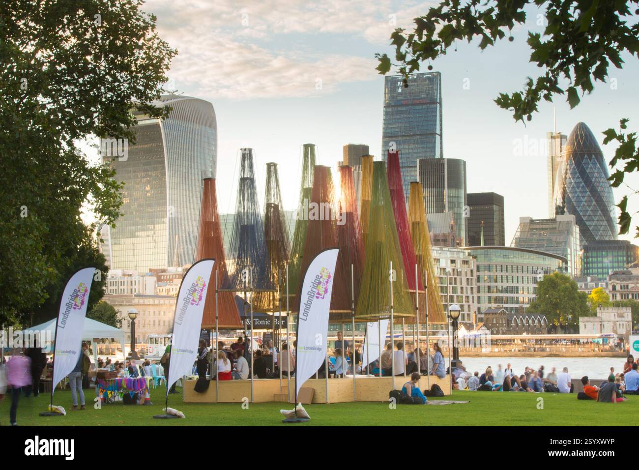 London Bridge, London. Die Menschen entspannen sich in einem Park und genießen eine London Bridge Live Arts Veranstaltung unter farbenfrohen Bauten. Stockfoto