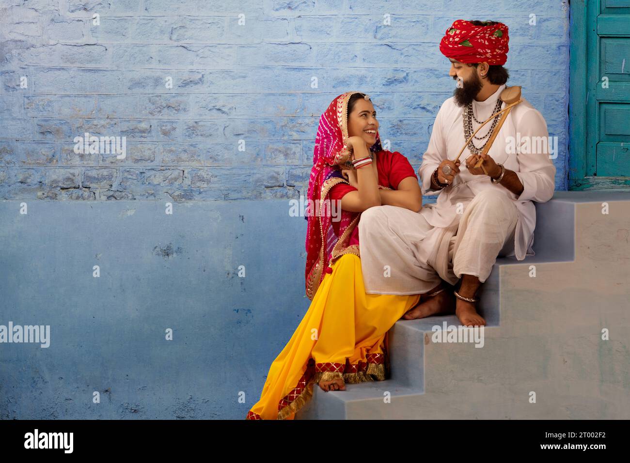 Rajasthani-Paar sitzt auf einer Treppe und teilt einen leichten Moment, während der Ehemann Ektara spielt Stockfoto