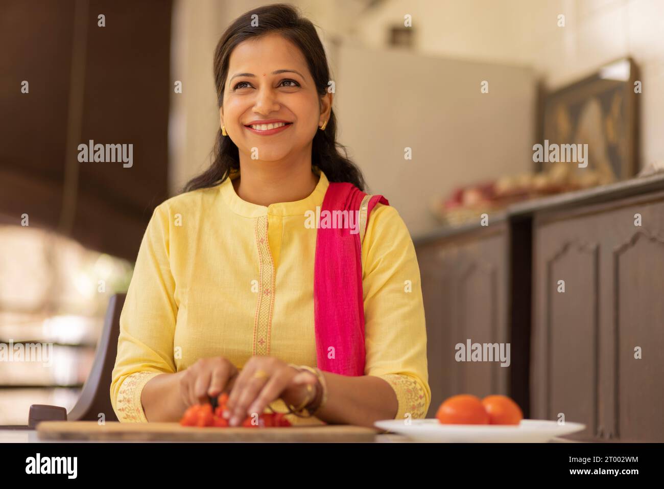 Lächelnde junge Frau, die zu Hause Gemüse hackt Stockfoto
