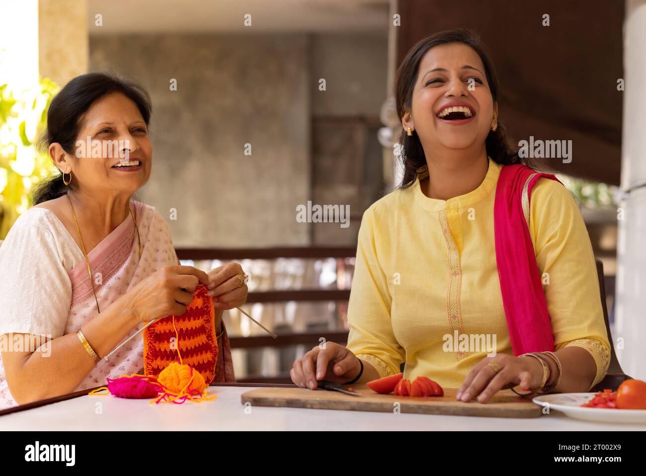Schwiegermutter und Schwiegertochter schauen mit einem Lächeln weg, während sie auf ihrem Balkon Hausarbeiten machen Stockfoto