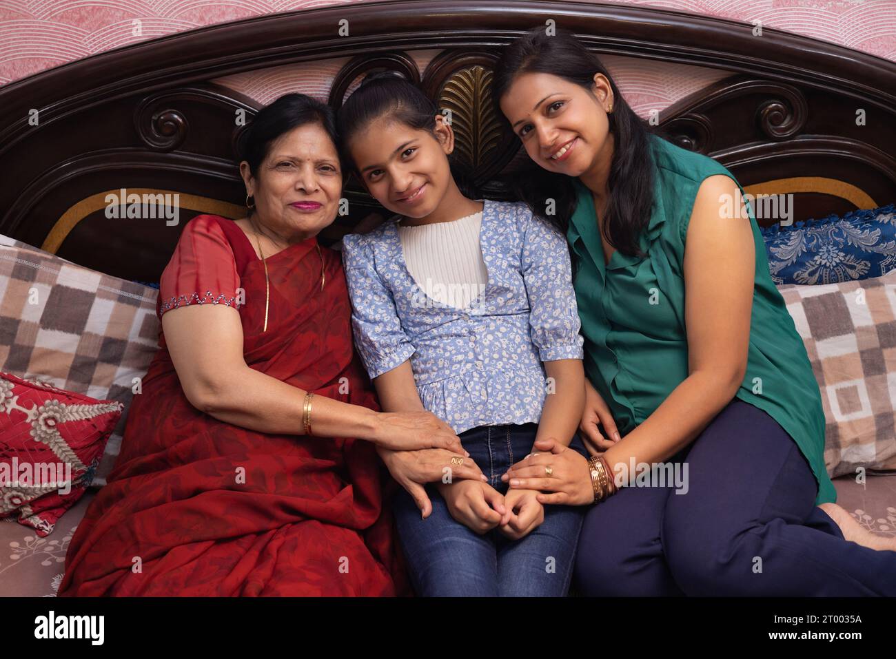 Indische Familie mit mehreren Generationen, die auf dem Bett im Schlafzimmer sitzt Stockfoto