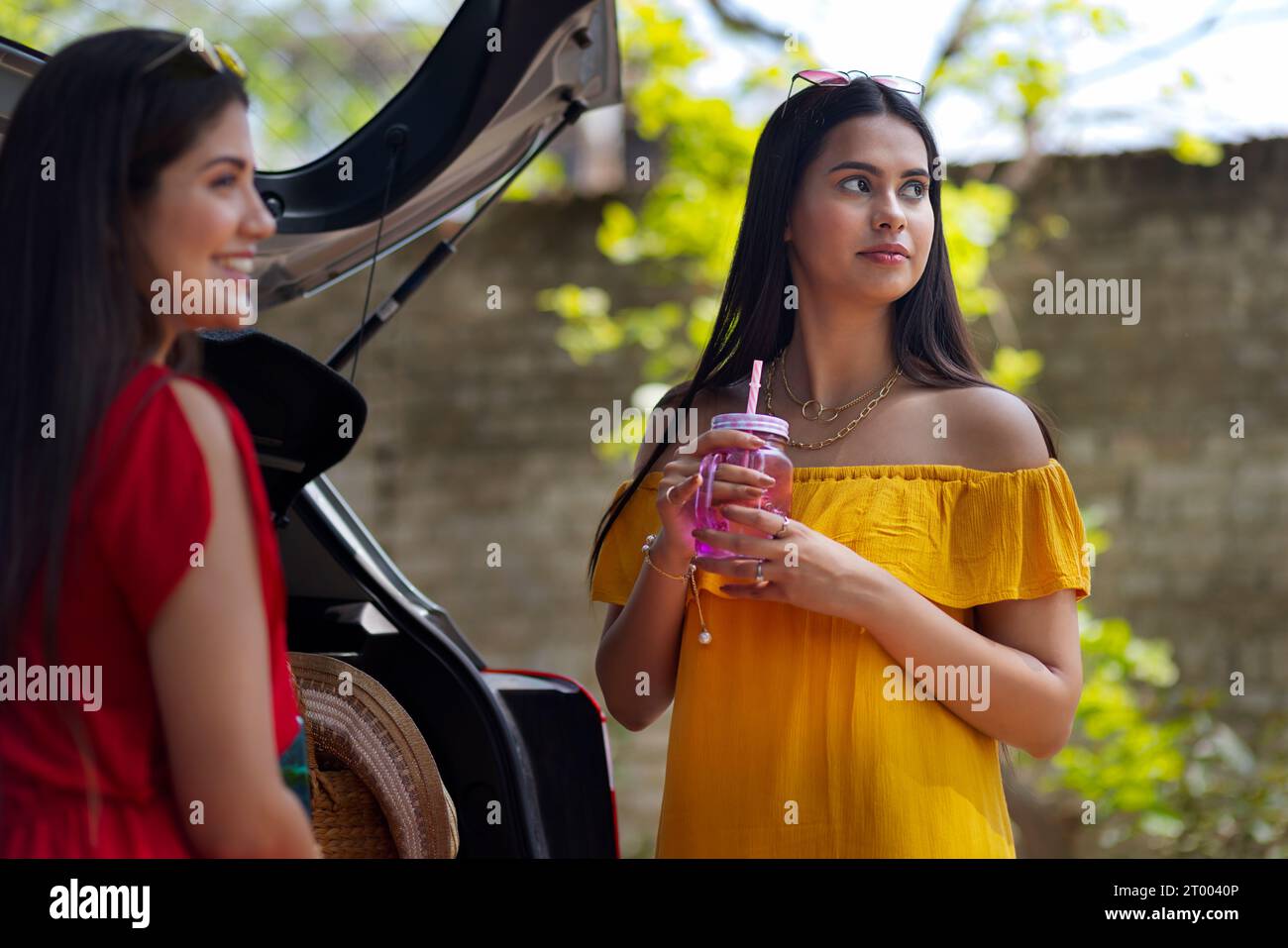 Zwei junge Frauen trinken Entgiftungswasser, während sie sich hinter einem Auto ausruhen Stockfoto