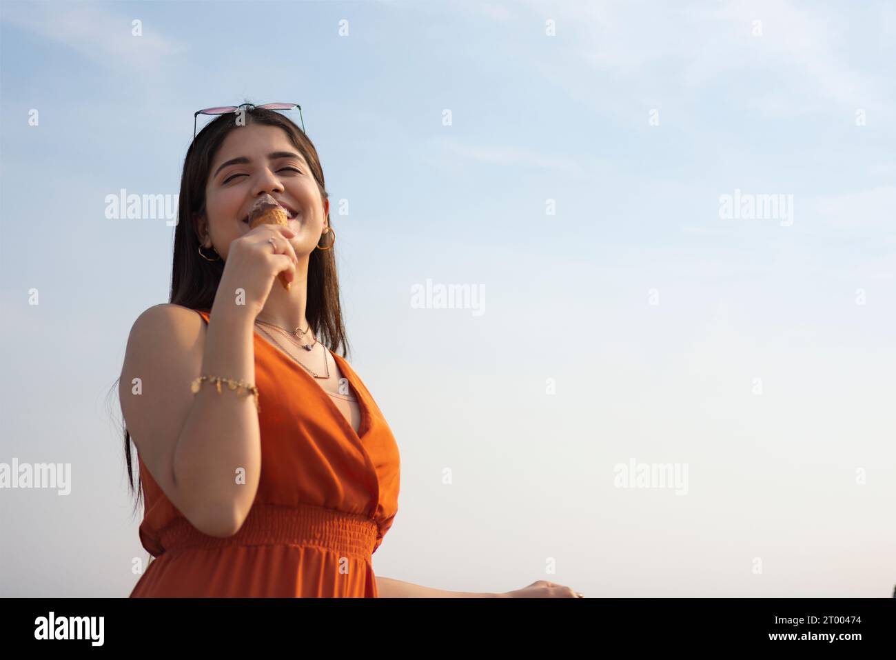 Porträt einer jungen Frau, die Eis im Kegel vor blauem Himmel isst Stockfoto
