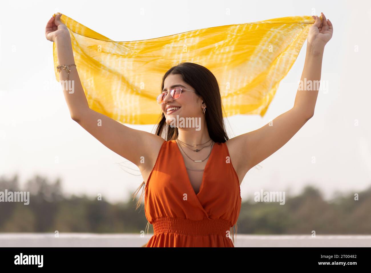 Schöne junge Dame, die am Strand steht und einen gelben Schal im Wind hält Stockfoto