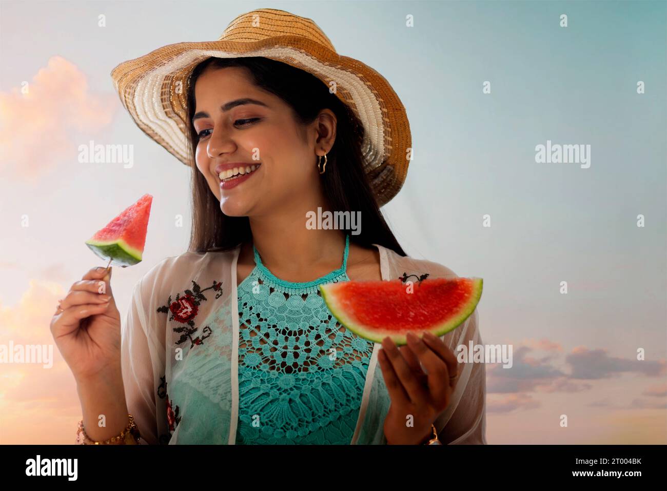 Lächelnde junge Frau mit Hut isst Wassermelone am Strand Stockfoto