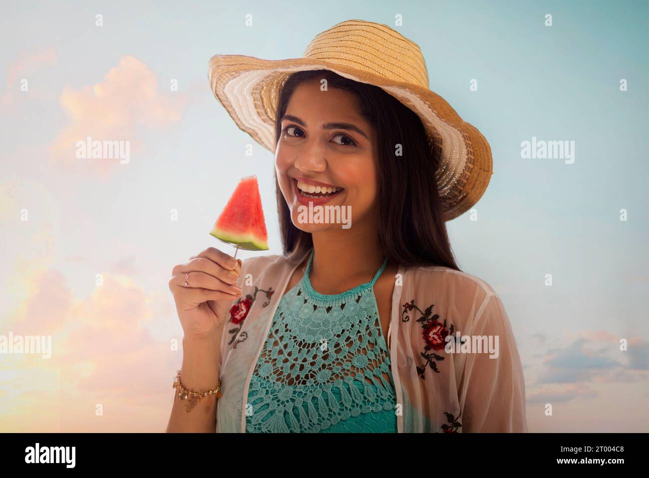 Lächelnde junge Frau mit Hut isst Wassermelone am Strand Stockfoto