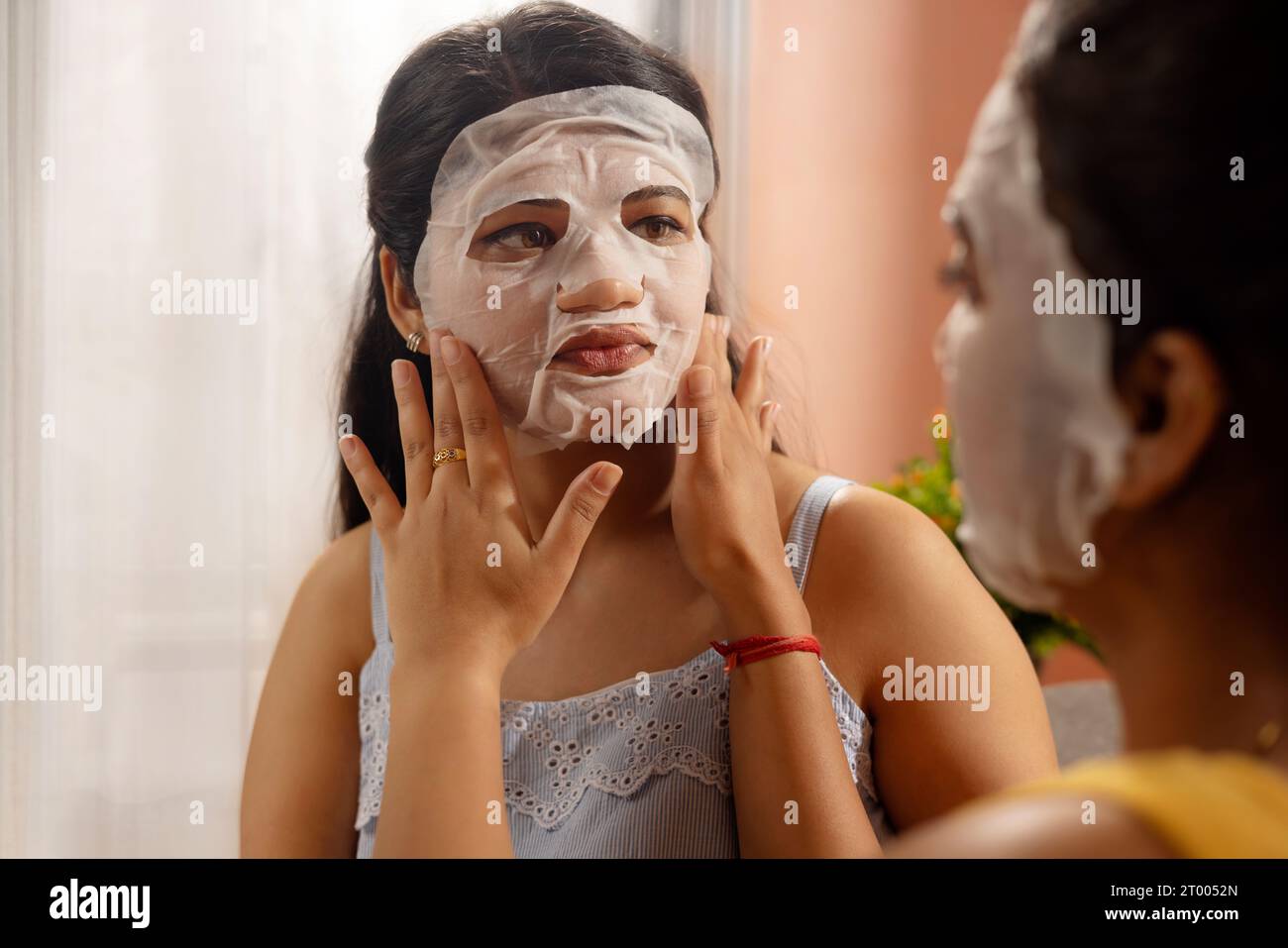 Frau, die im Wohnzimmer eine Gesichtsmaske auf das Gesicht ihres Freundes aufträgt Stockfoto