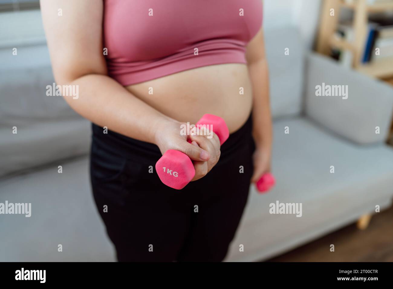 Übergewichtige Frau, die zur Gewichtsreduktion trainiert. Sport mit Kurzhanteln in Stretchpositionen zu Hause im Wohnzimmer fröhlich Stockfoto