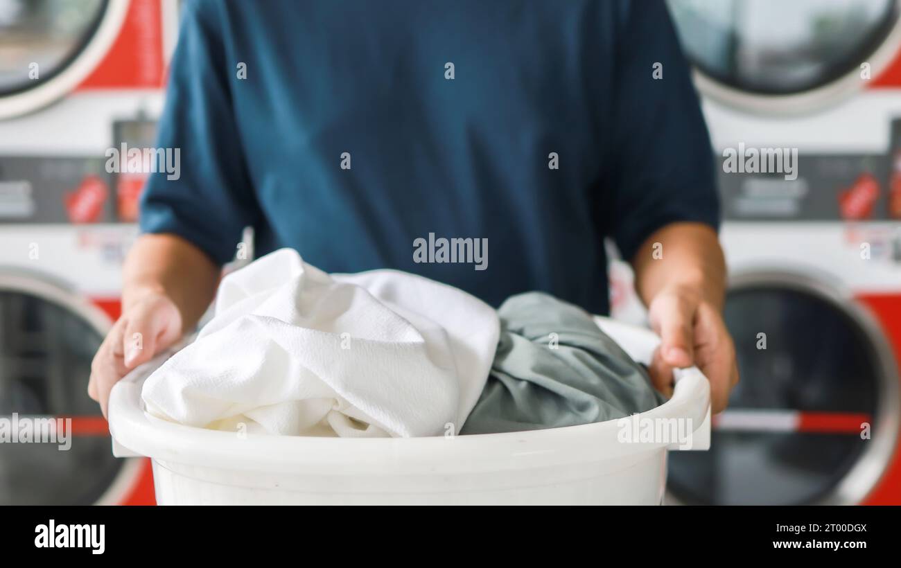 Hausmann mit Korb und schmutziger laundryÂ gewaschener Kleidung im Waschraum. Waschen machineÂ im Wäschereigeschäft Stockfoto