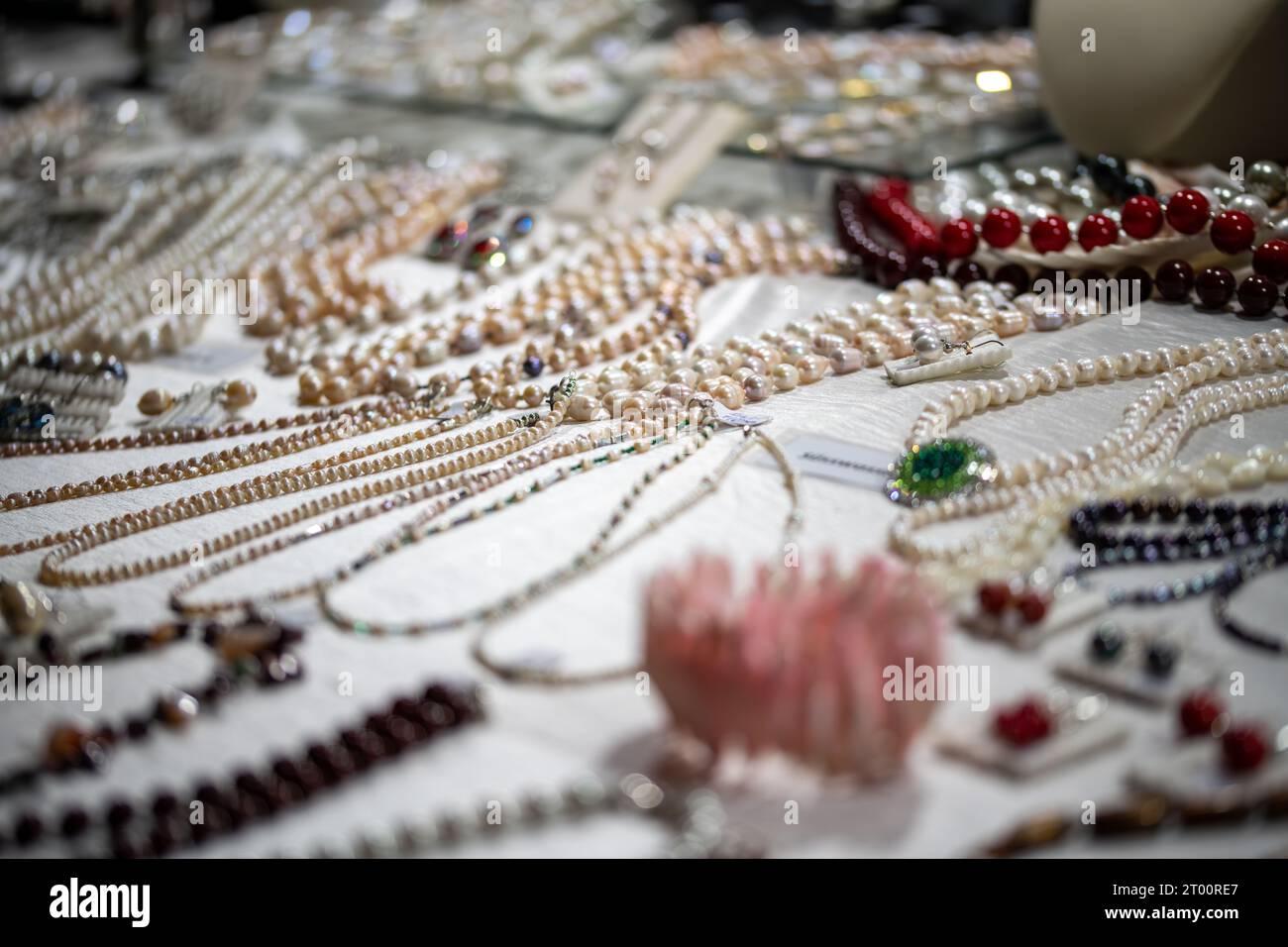Viele Halsketten und Ohrringe auf verschiedenen Materialien auf einer Oberfläche wunderschön in dezentem Licht drapiert Stockfoto