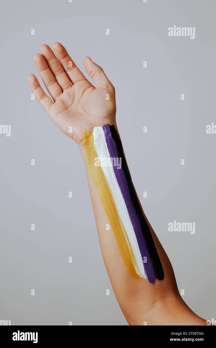 Nahaufnahme des Arms einer Person mit der nicht-binären Stolz-Fahne, die darin gemalt ist, vor einem hellgrauen Hintergrund Stockfoto